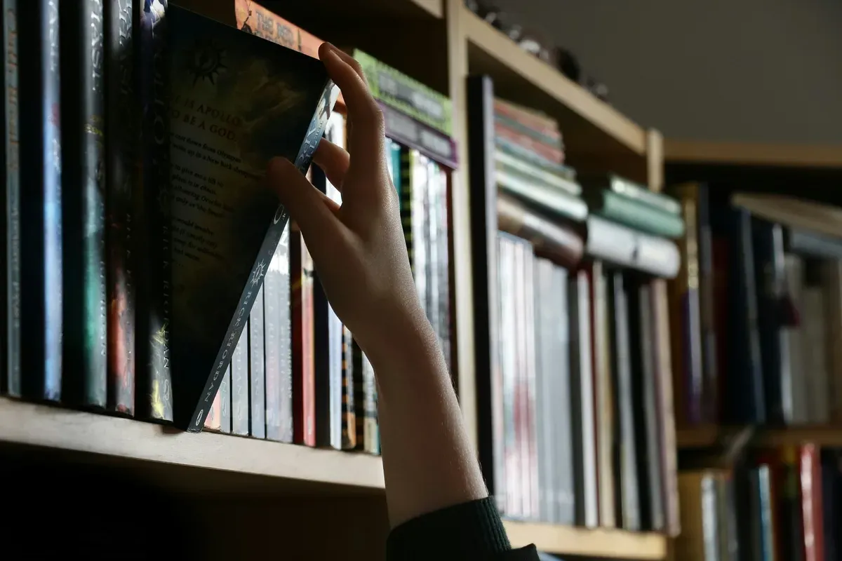 Una mano sfila un libro da uno scaffale di una biblioteca.