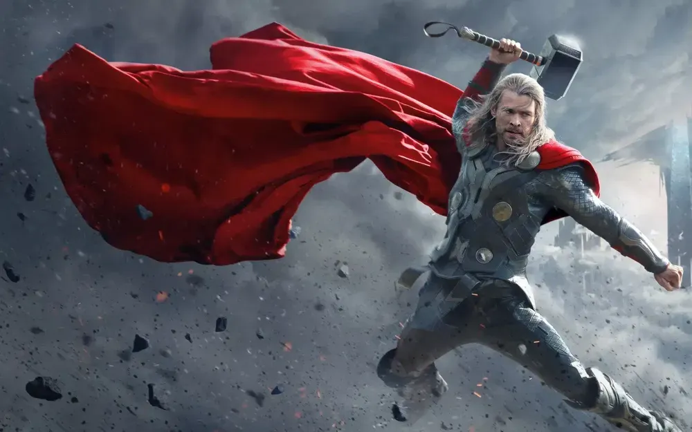 A fictional male character with long hair and a red cloak wields a hammer in a dramatic setting, surrounded by debris and smoke.