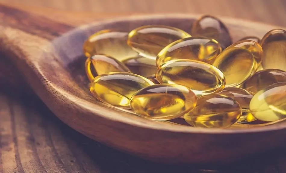 Capsule di vitamina D3 in una cucchiaia di legno, utilizzate per supportare la salute ossea e il benessere generale.